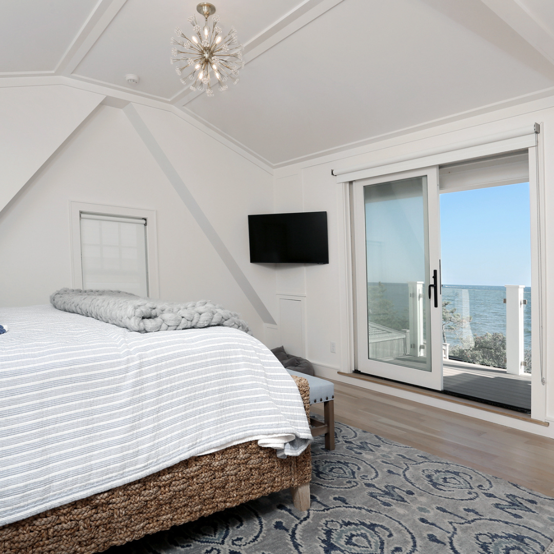 Elegant coastal master bedroom with ocean view, featuring sliding glass doors leading to a private balcony in a Cape Cod waterfront home designed by Encore Construction.