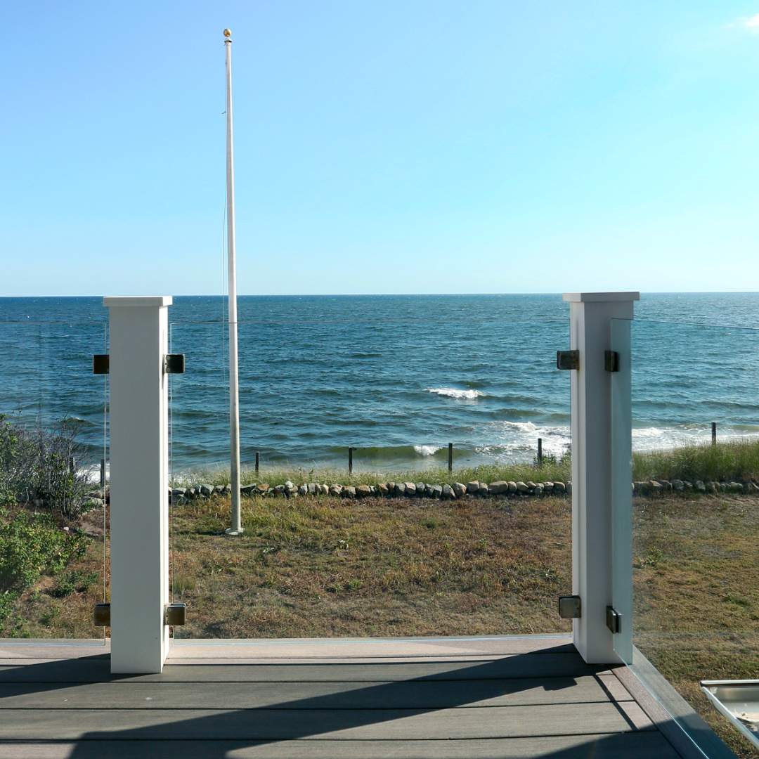 View from a coastal home’s deck overlooking the ocean, featuring a glass-paneled railing and unobstructed seaside landscape, part of a Cape Cod waterfront renovation by Encore Construction.